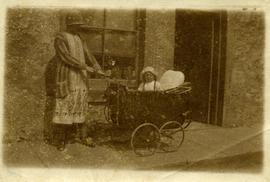 Woman with young child in pram in front of shop.